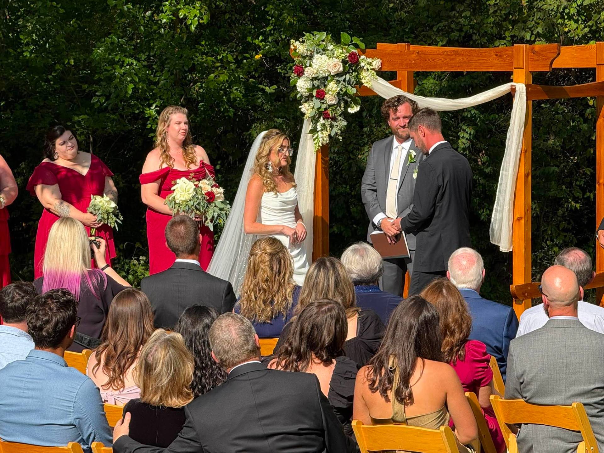 Outdoor wedding ceremony with red bridesmaid dresses and floral arch